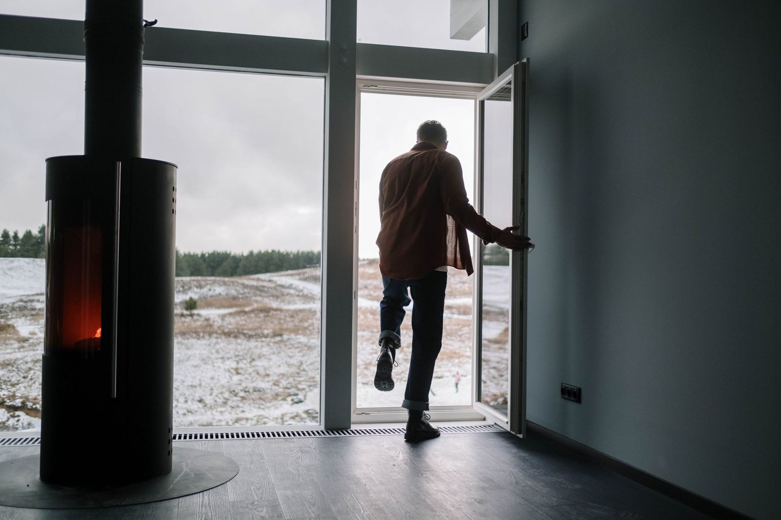 A person by a large window with a wood stove on a snowy day