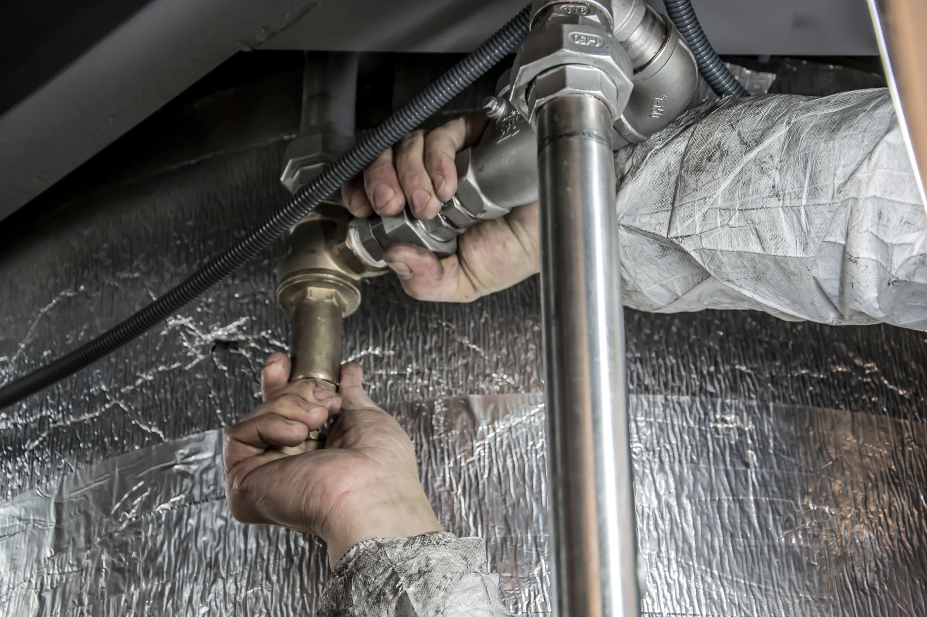 A hand checking an outdoor spigot valve in fall